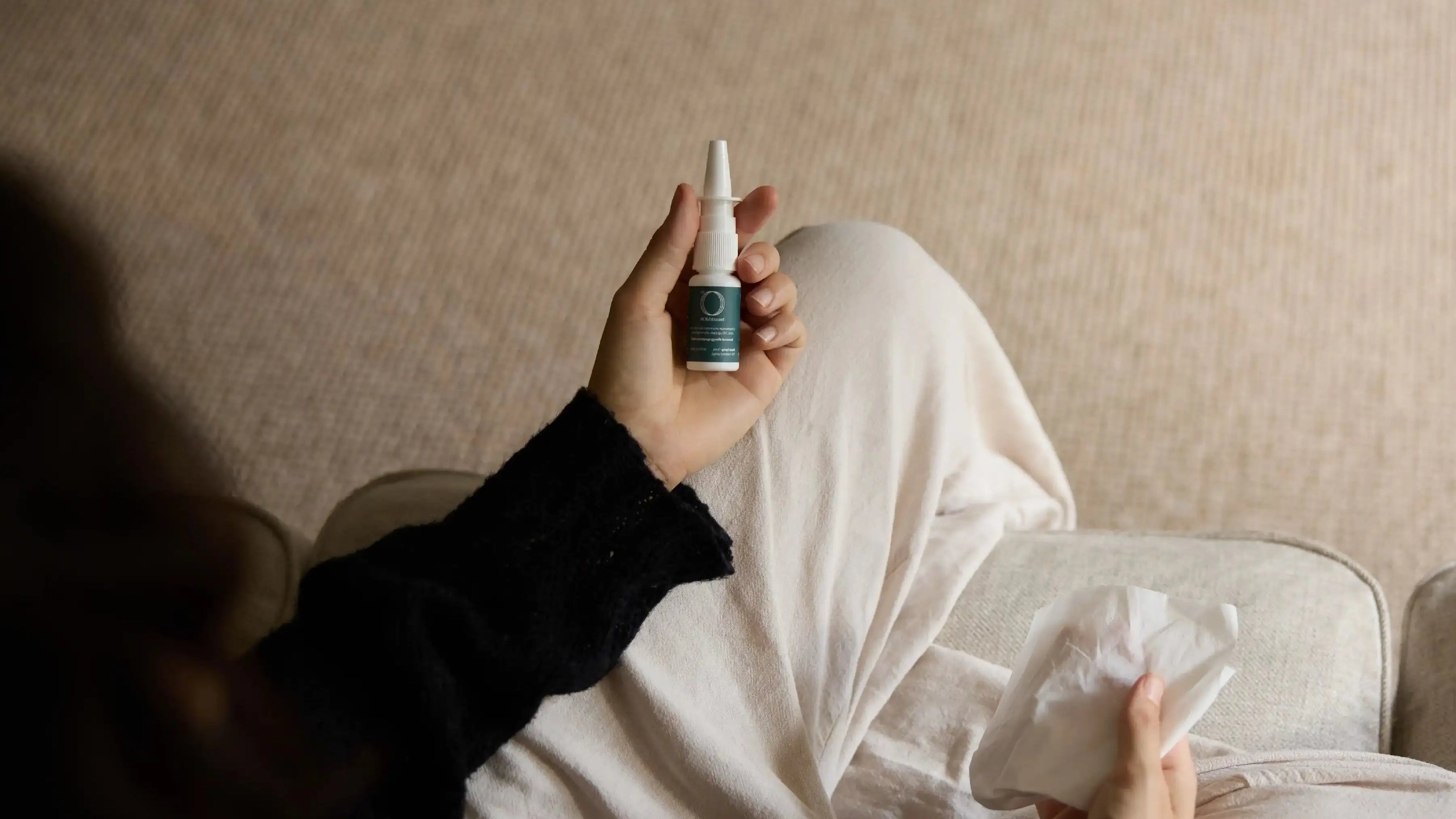 Person holding a nasal spray bottle of BreathMOR and tissue on a couch.