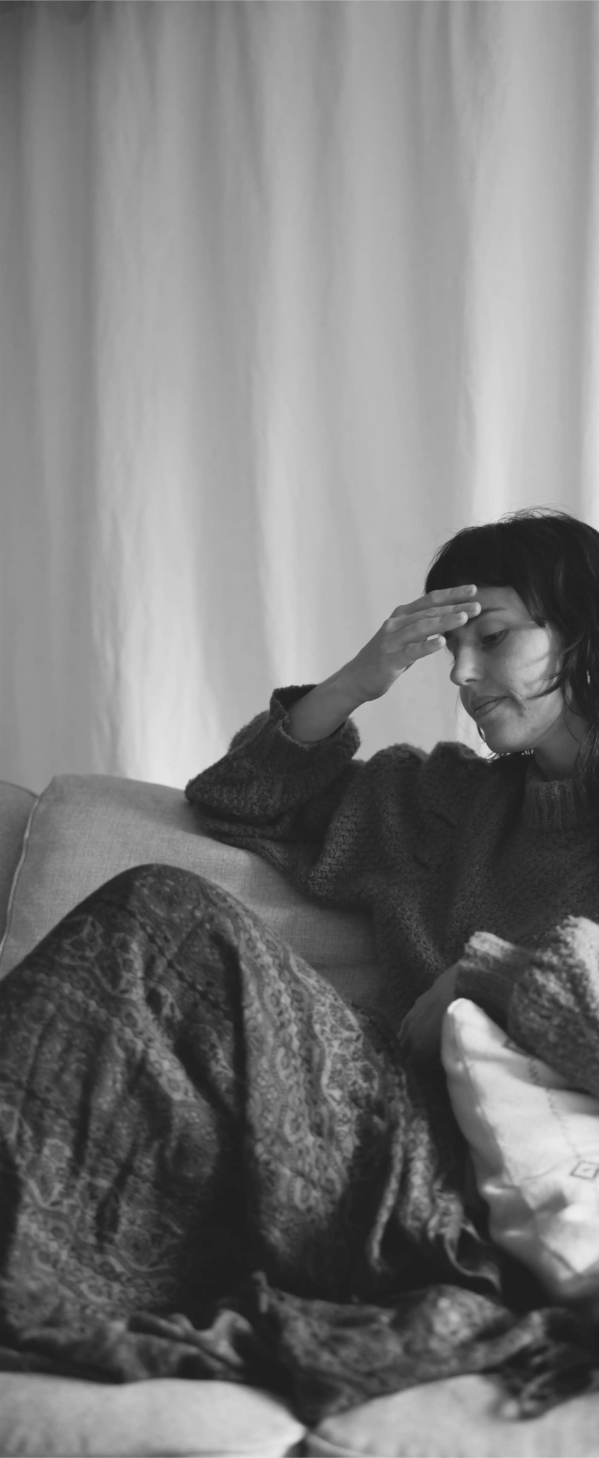 Person sitting on a couch with a blanket, looking contemplative.