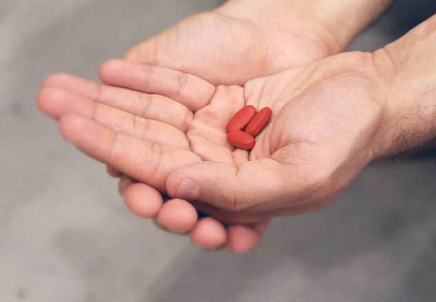 Hand holding three red pills against a gray background
