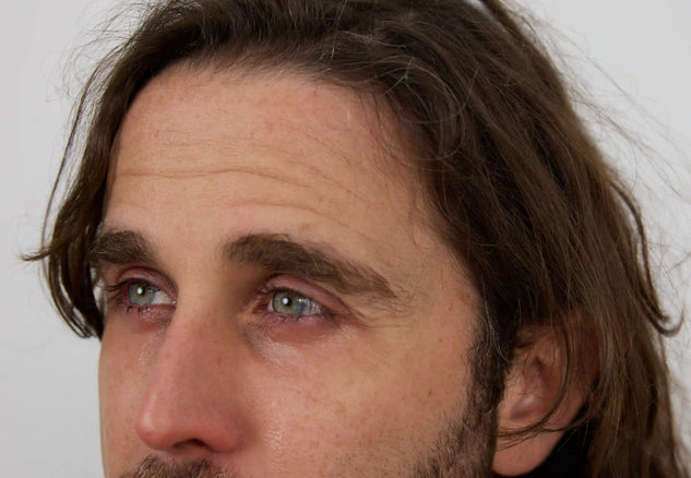 Close-up of a man with long hair and beard against a plain background