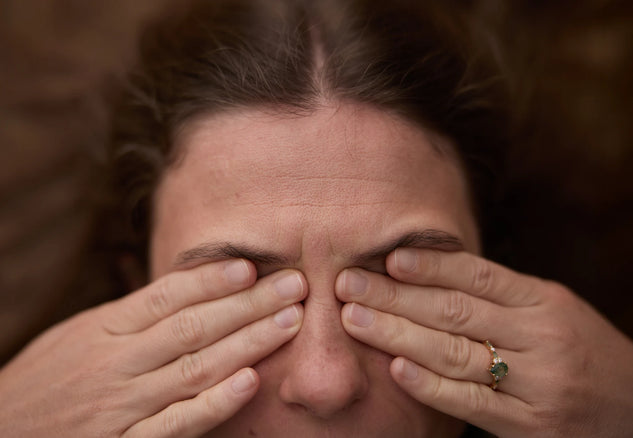 Person covering their eyes with their hands against a blurred background