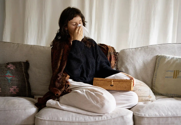 Person sitting on a couch with a blanket, tissue, and wooden box in a home setting.