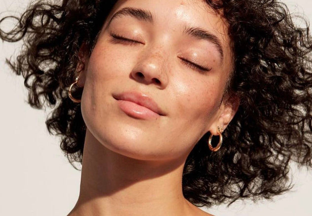 Woman with closed eyes and wavy hair against a neutral background